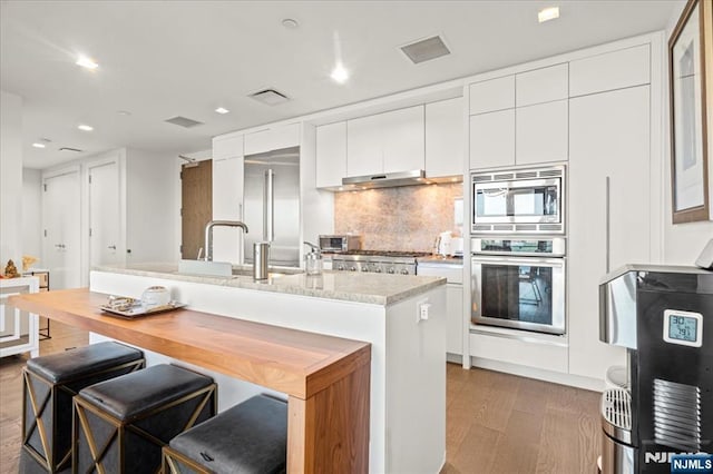 320 Adolphus Ave Unit 317, Cliffside Park, NJ 07010 - kitchen with built in appliances, under cabinet range hood, decorative backsplash, white cabinetry, and an island with sink