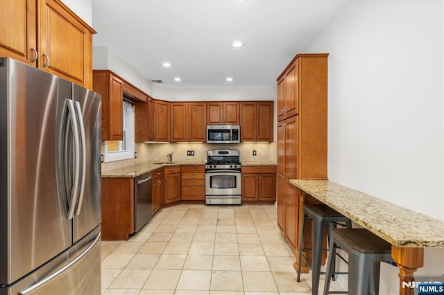 211 Harrison Ave, Hasbrouck Heights, NJ 07604 - kitchen featuring appliances with stainless steel finishes, light stone counters, brown cabinetry, backsplash, and a peninsula