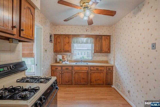 11 Newman Ave, Nutley, NJ 07110 - kitchen featuring white gas range oven, wallpapered walls, brown cabinets, a sink, and light wood-style floors
