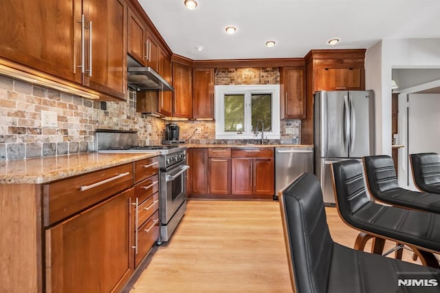 28 Elizabeth Ct, Secaucus, NJ 07094 - kitchen featuring appliances with stainless steel finishes, extractor fan, light wood finished floors, light stone counters, and backsplash