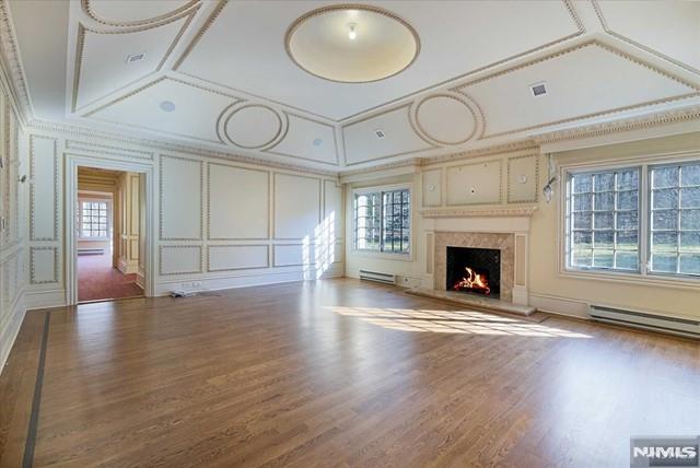 11 Margo Way, Alpine, NJ 07620 - unfurnished living room featuring a decorative wall, a baseboard radiator, wood finished floors, crown molding, and a premium fireplace