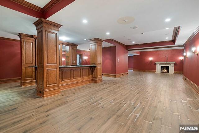 11 Margo Way, Alpine, NJ 07620 - unfurnished living room featuring ornate columns, crown molding, light wood finished floors, a warm lit fireplace, and recessed lighting