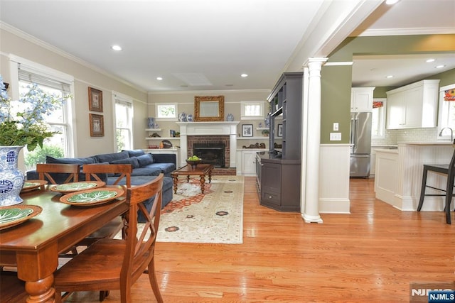  - living area with crown molding, light wood-type flooring, a brick fireplace, ornate columns, and recessed lighting