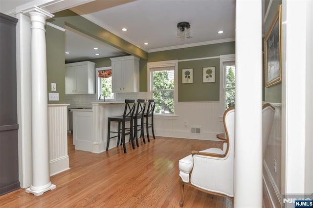  - kitchen with ornate columns, a breakfast bar, a wainscoted wall, light wood-style flooring, and ornamental molding