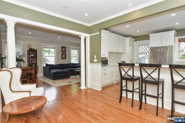  - kitchen featuring appliances with stainless steel finishes, decorative columns, white cabinets, light wood-type flooring, and ornamental molding