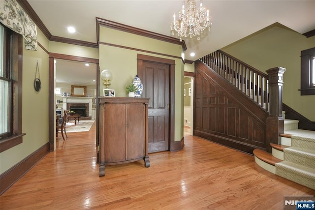  - foyer entrance with ornamental molding, stairs, light wood-style floors, a chandelier, and a fireplace with raised hearth