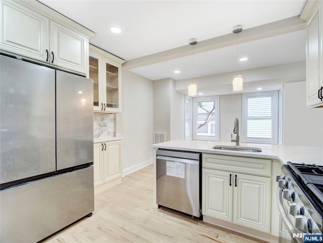 138 Willow St, Bloomfield, NJ 07003 - kitchen featuring appliances with stainless steel finishes, light countertops, light wood-style floors, pendant lighting, and glass insert cabinets