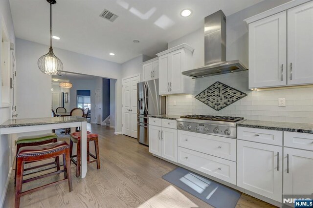 178 Arthur St, Hillsdale, NJ 07642 - kitchen featuring wall chimney exhaust hood, stainless steel appliances, white cabinetry, a breakfast bar, and dark stone counters