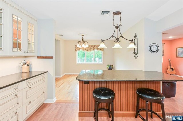 16 Murray Rd, Montvale, NJ 07645 - kitchen featuring a breakfast bar area, light wood finished floors, glass insert cabinets, dark stone countertops, and hanging light fixtures