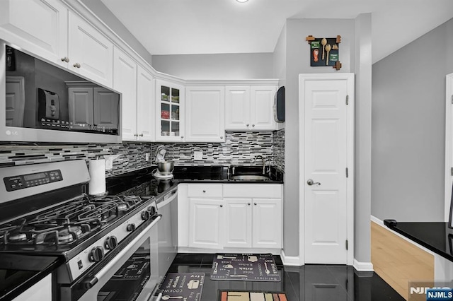 303 Wilshire Dr, Nutley, NJ 07110 - kitchen featuring appliances with stainless steel finishes, white cabinets, backsplash, dark countertops, and glass insert cabinets