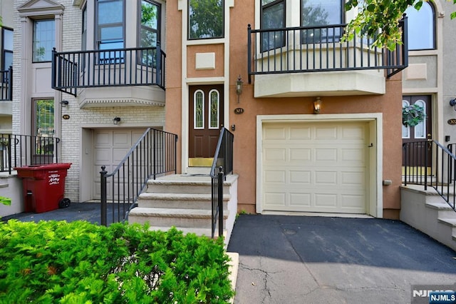 303 Wilshire Dr, Nutley, NJ 07110 - property entrance featuring asphalt driveway, an attached garage, a balcony, and stucco siding