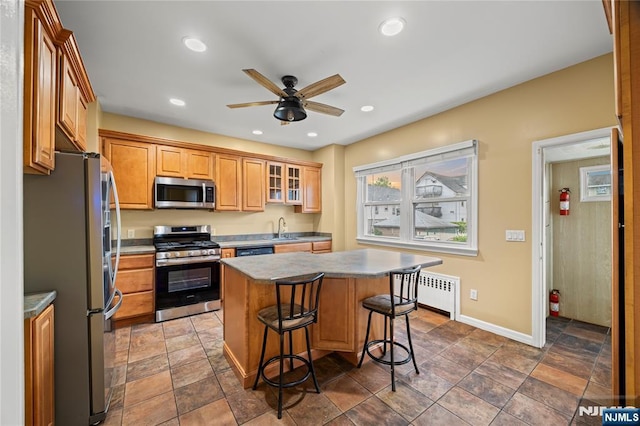 115 12th St, Prospect Park, NJ 07508 - kitchen with appliances with stainless steel finishes, radiator heating unit, a kitchen bar, a ceiling fan, and a kitchen island