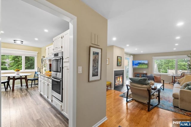 206 Wind Hollow Ct, Mahwah, NJ 07430 - kitchen with stainless steel double oven, open floor plan, a fireplace with flush hearth, white cabinetry, and healthy amount of natural light