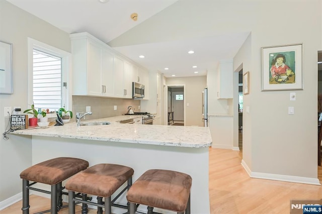 39 Terrace Rd, Wayne, NJ 07470 - kitchen featuring appliances with stainless steel finishes, a peninsula, white cabinetry, light wood-style floors, and a kitchen bar