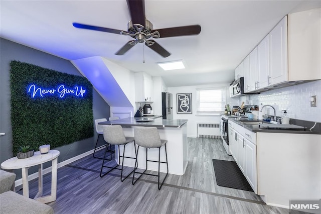 71 Pickens St, Little Ferry, NJ 07643 - kitchen with electric range oven, radiator heating unit, dark countertops, a breakfast bar, and a peninsula