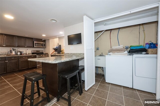71 Pickens St, Little Ferry, NJ 07643 - kitchen with stainless steel appliances, washer and clothes dryer, dark brown cabinetry, a kitchen bar, and dark tile patterned flooring