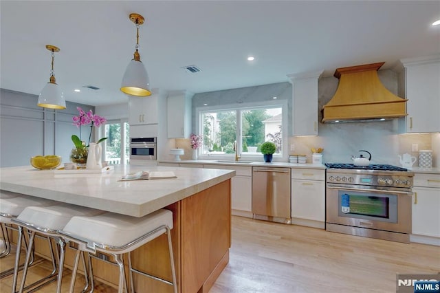 415 Bailey Rd, Paramus, NJ 07652 - kitchen featuring stainless steel appliances, custom exhaust hood, white cabinets, backsplash, and decorative light fixtures