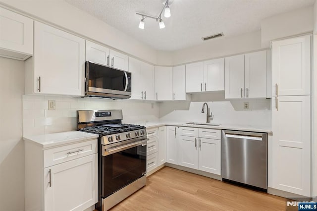 7 Eakens Ct, Mahwah, NJ 07430 - kitchen featuring appliances with stainless steel finishes, white cabinets, light wood-type flooring, decorative backsplash, and a textured ceiling