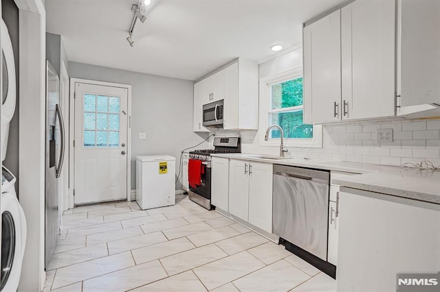 2 Ann St, Bloomingdale, NJ 07403 - kitchen featuring appliances with stainless steel finishes, stacked washing machine and dryer, backsplash, white cabinets, and track lighting