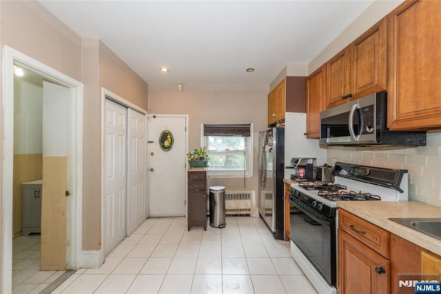 23 Preston St, Ridgefield Park, NJ 07660 - kitchen with stainless steel appliances, radiator, brown cabinets, light tile patterned flooring, and light countertops