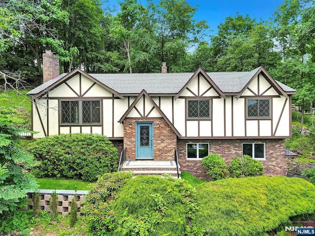 6 Hazel St, Woodland Park, NJ 07424 - tudor-style house featuring stucco siding, a chimney, brick siding, roof with shingles, and view of scattered trees