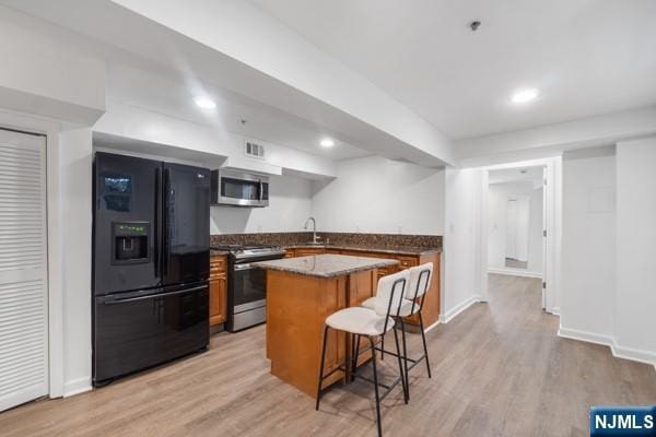 2608 Kennedy Blvd Unit 1, Union City, NJ 07087 - kitchen featuring appliances with stainless steel finishes, a center island, light wood-style floors, a breakfast bar, and brown cabinets