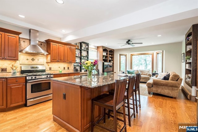 34 Harding Rd, Glen Rock, NJ 07452 - kitchen with stainless steel gas range oven, wall chimney range hood, light wood finished floors, dark stone countertops, and a kitchen breakfast bar