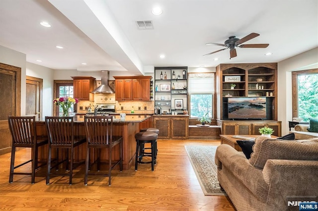 34 Harding Rd, Glen Rock, NJ 07452 - kitchen featuring wall chimney exhaust hood, a breakfast bar area, light wood-style flooring, a ceiling fan, and an island with sink