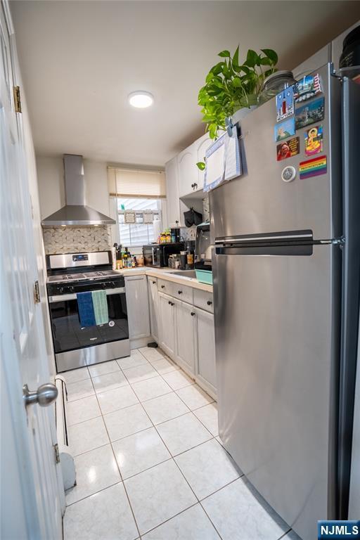 95 Mount Prospect Ave, Newark, NJ 07104 - kitchen with appliances with stainless steel finishes, wall chimney range hood, light tile patterned floors, light countertops, and white cabinets