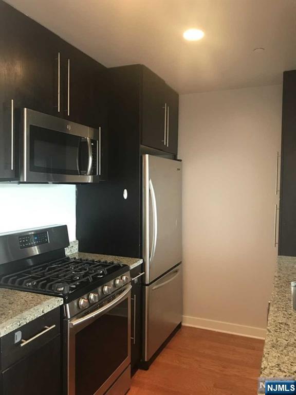 1611 Hudson Park Unit 1611, Edgewater, NJ 07020 - kitchen with appliances with stainless steel finishes, dark cabinetry, light wood-style floors, and light stone countertops