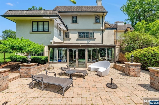 82 Jackson Dr, Cresskill, NJ 07626 - rear view of property featuring stucco siding, a sunroom, a patio, a chimney, and roof with shingles