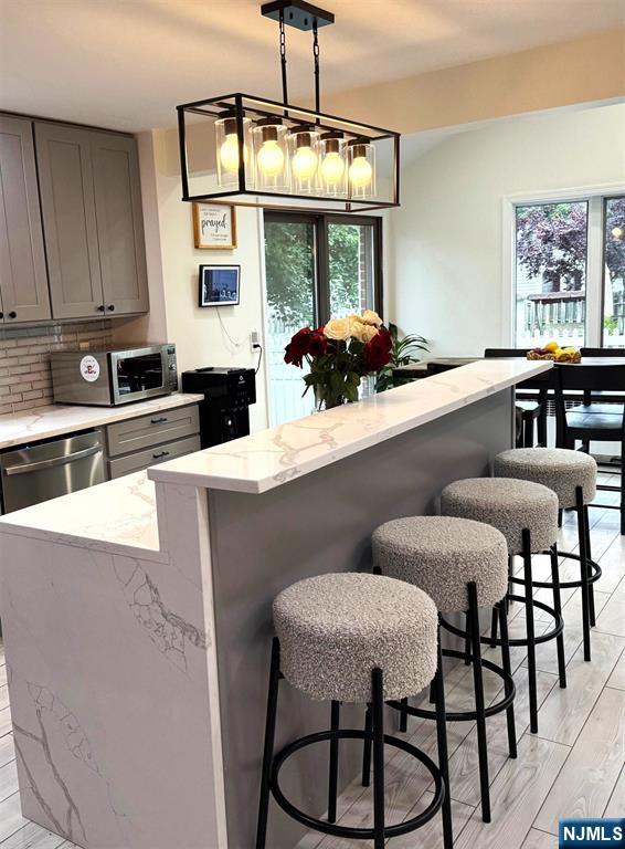 45 Highland Ave, Emerson, NJ 07630 - kitchen featuring appliances with stainless steel finishes, gray cabinets, a breakfast bar, a kitchen island, and light stone counters
