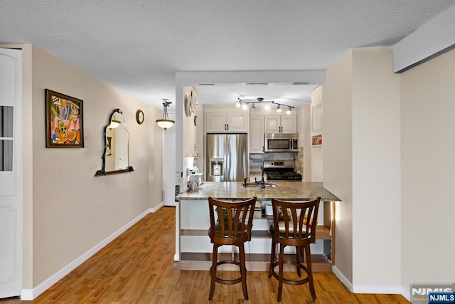 555 N Ave Unit 15W, Fort Lee, NJ 07024 - kitchen with stainless steel appliances, a peninsula, decorative backsplash, white cabinets, and light wood finished floors