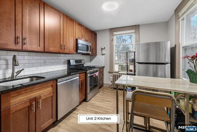 87 James St, Englewood, NJ 07631 - kitchen featuring appliances with stainless steel finishes, radiator, dark stone counters, light wood-style floors, and tasteful backsplash
