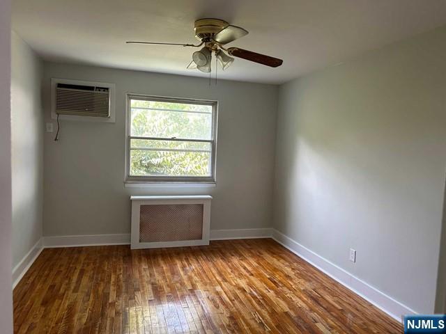125 E Clinton Unit 10B, Bergenfield, NJ 07621 - empty room with a wall mounted AC, radiator heating unit, ceiling fan, and hardwood / wood-style floors