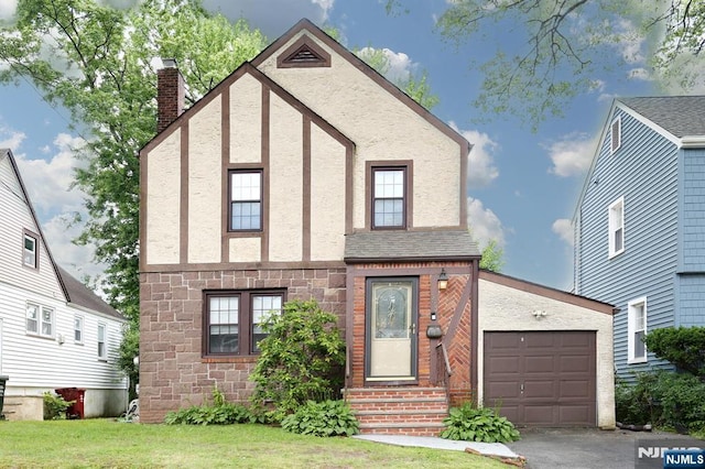 393 High St, Nutley, NJ 07110 - tudor home featuring entry steps, stone siding, a chimney, a front yard, and an attached garage