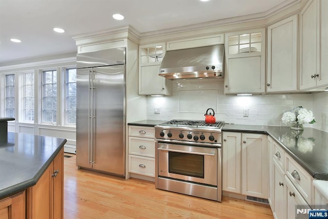 152 Highwood Ave, Tenafly, NJ 07670 - kitchen featuring premium appliances, wall chimney exhaust hood, dark countertops, light wood-type flooring, and decorative backsplash