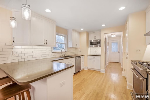37 Franklin St, Cedar Grove, NJ 07009 - kitchen with appliances with stainless steel finishes, a breakfast bar, a peninsula, white cabinets, and light wood-style flooring
