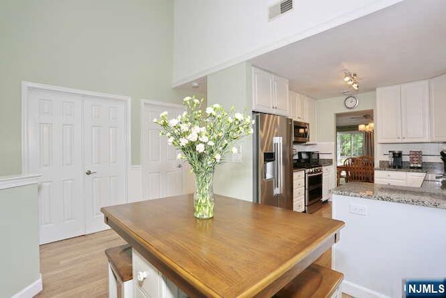 84 Pheasant Run Unit 84, Old Tappan, NJ 07675 - kitchen with stainless steel appliances, white cabinets, light wood-type flooring, stone counters, and a high ceiling