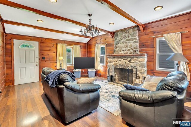 76 Hillside Rd, Sparta, NJ 07871 - living room featuring wood walls, a chandelier, wood finished floors, beam ceiling, and a stone fireplace