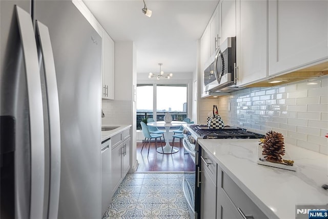 2077 Center Ave Unit 19C, Fort Lee, NJ 07024 - kitchen with stainless steel appliances, a chandelier, decorative backsplash, light stone countertops, and white cabinets