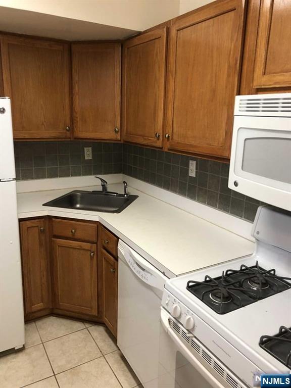 285 Aycrigg Ave Unit 22D, Passaic, NJ 07055 - kitchen with white appliances, tasteful backsplash, light tile patterned flooring, light countertops, and brown cabinetry