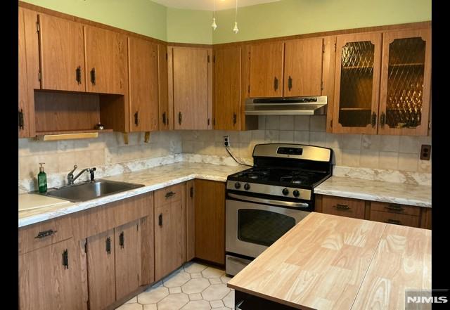 67 Melody Hill Rd, Clifton, NJ 07013 - kitchen featuring stainless steel range with gas cooktop, under cabinet range hood, tasteful backsplash, glass insert cabinets, and brown cabinets