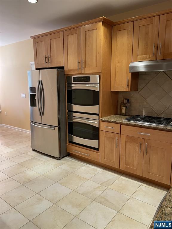 5 Cliff Rd Unit C1, Woodland Park, NJ 07424 - kitchen with appliances with stainless steel finishes, under cabinet range hood, brown cabinetry, tasteful backsplash, and dark stone countertops