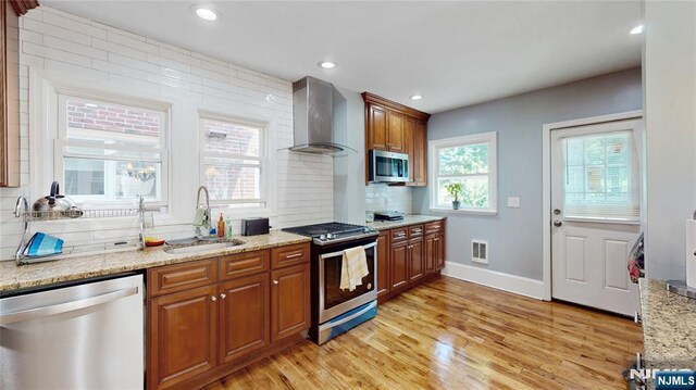 39 Boyden Pkwy, Maplewood, NJ 07040 - kitchen featuring stainless steel appliances, wall chimney range hood, light wood-style flooring, brown cabinets, and decorative backsplash
