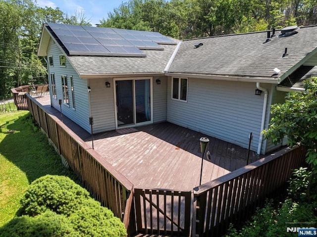 699 Shore Rd, West Milford, NJ 07421 - rear view of property with roof mounted solar panels, a wooden deck, roof with shingles, and a lawn