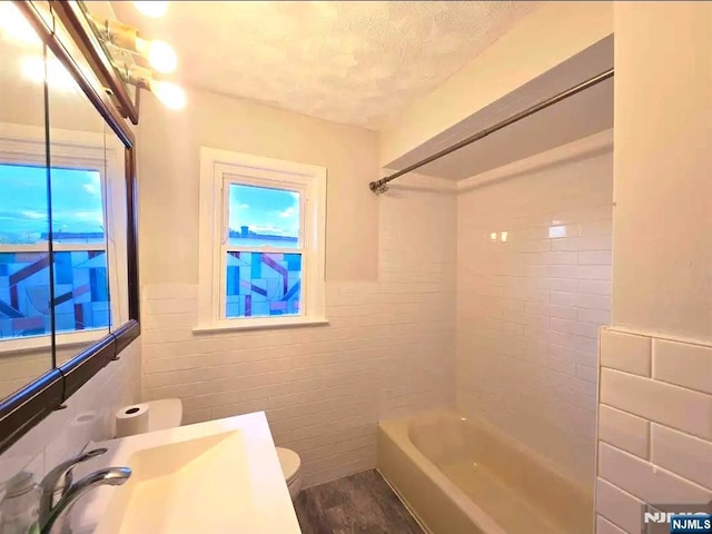 137 Prospect St, Lodi, NJ 07644 - full bathroom with shower / washtub combination, a textured ceiling, wood finished floors, a wainscoted wall, and tile walls