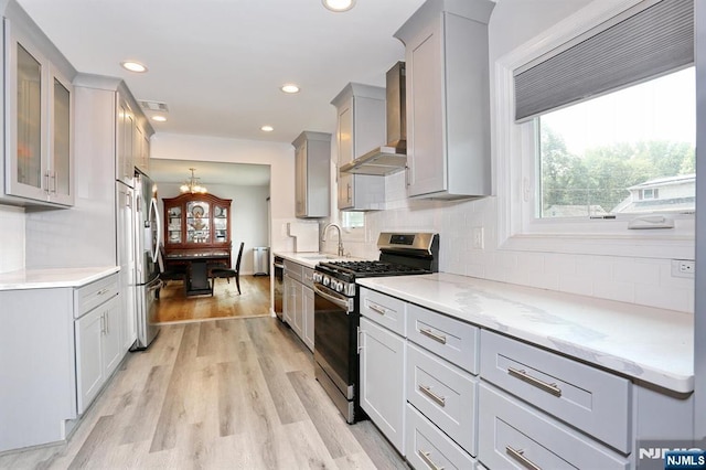 8 Cedar Rd, Dumont, NJ 07628 - kitchen with appliances with stainless steel finishes, wall chimney exhaust hood, a chandelier, light wood-style flooring, and decorative backsplash