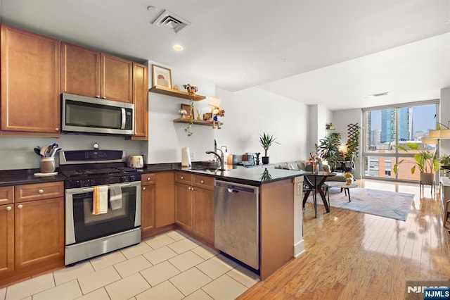 201 Marin Blvd Unit 1209, Jersey City, NJ 07302 - kitchen featuring appliances with stainless steel finishes, dark countertops, brown cabinets, a peninsula, and open shelves