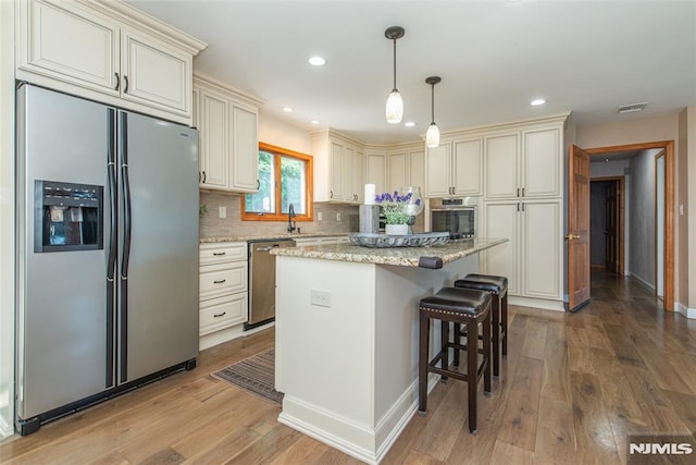 44 Columbus Ave, Totowa, NJ 07512 - kitchen with appliances with stainless steel finishes, cream cabinetry, decorative backsplash, wood finished floors, and light stone countertops